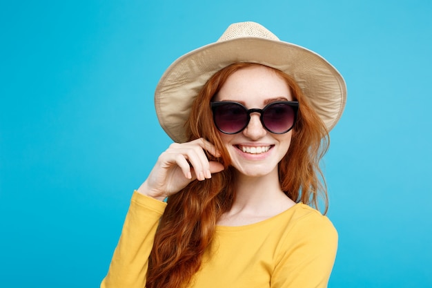 Reise-Konzept - Close up Portrait junge schöne attraktive Ingwer rote Haare Mädchen mit trendy Hut und Sonnenbrille lächelnd. Blauer Pastellhintergrund. Platz kopieren