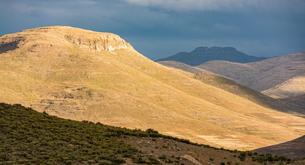 Reise nach Lesotho Die Sonne erleuchtet einen Berg, während der Sturm aufzieht