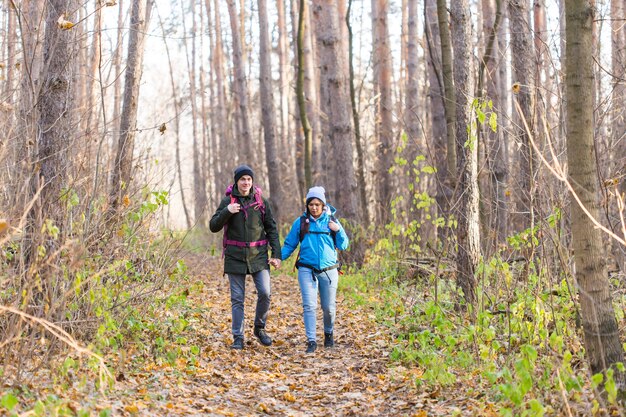 Reise-, Tourismus-, Wander- und Naturkonzept - Touristen, die mit einem Rucksack in blauen und schwarzen Jacken im Park spazieren gehen.