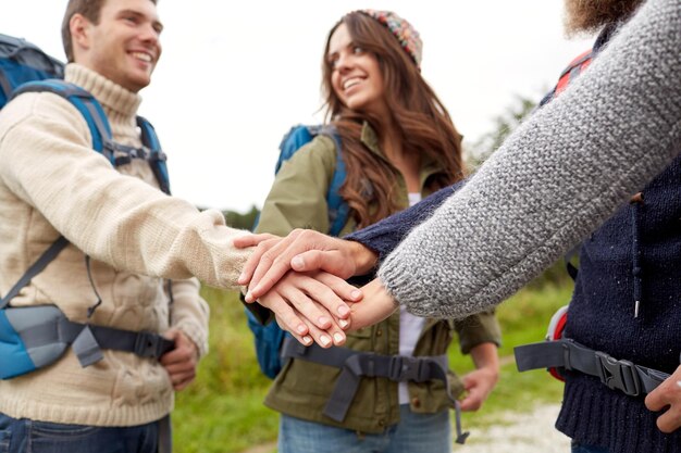 Foto reise-, tourismus-, wanderungs-, gesten- und personenkonzept - gruppe lächelnder freunde mit rucksäcken, die hände übereinander legen