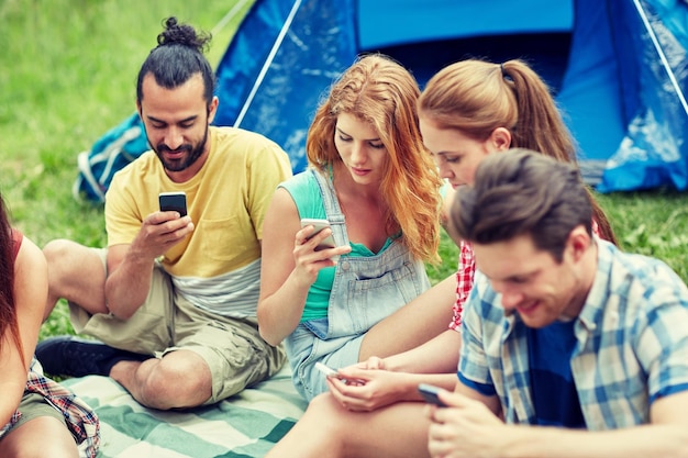 reise-, tourismus-, wanderungs-, technologie- und personenkonzept - gruppe von freunden mit smartphone und zelt beim camping