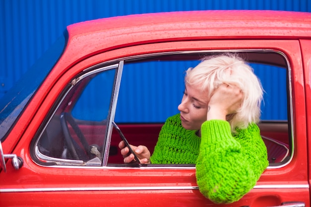 Foto reise- und modekonzept mit attraktiven menschen dame kaukasier in einem roten retro-schönen auto mit handy-internet verbunden, um karte zu überprüfen und neue orte zu entdecken farben bild.