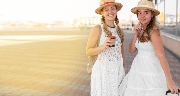 Reise- und Tourismuskonzept. Zwei schöne und fröhliche Mädchen-Touristen mit Mützen und Kaffee zum Mitnehmen.