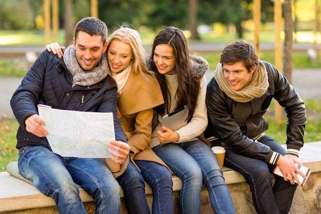 reise-, urlaubs-, menschen-, tourismus- und freundschaftskonzept - gruppe lächelnder freunde, die mit tablet-pc-stadtführer und karte im park sitzen