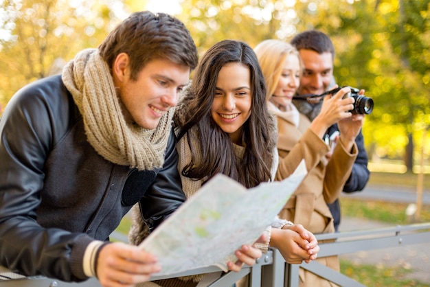 reise-, urlaubs-, technologie-, tourismus- und freundschaftskonzept - gruppe lächelnder freunde mit digitaler fotokamera und karte im stadtpark