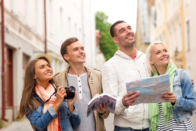 reise-, urlaubs-, technologie- und freundschaftskonzept - gruppe lächelnder freunde mit stadtführer, fotokamera und karte, die die stadt erkunden