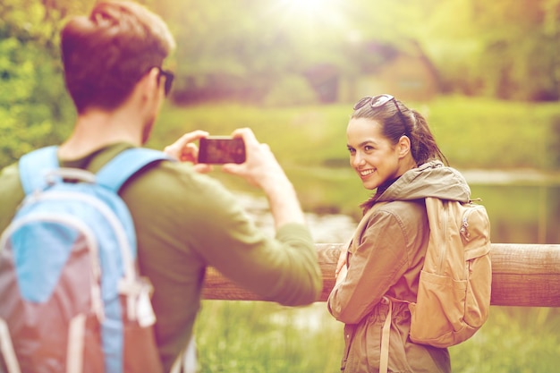 Reise-, Wander-, Rucksackreisen-, Tourismus- und Personenkonzept - lächelndes Paar mit Rucksäcken, das mit dem Smartphone in der Natur fotografiert