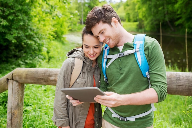 Reise-, Wander-, Rucksackreisen-, Tourismus- und Personenkonzept - lächelndes Paar mit Rucksäcken und Tablet-PC-Computer in der Natur