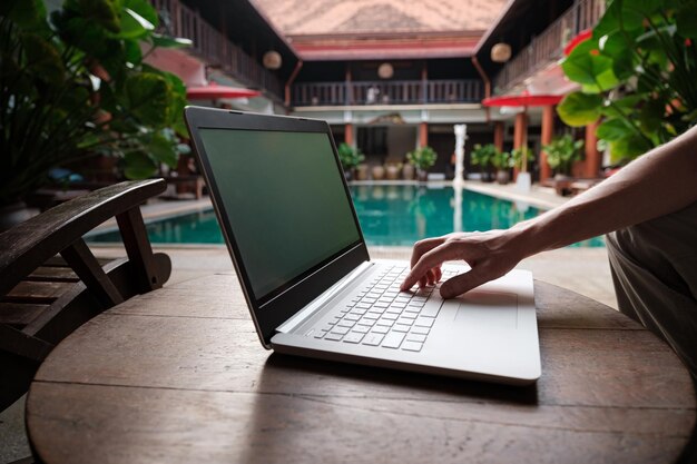 Reiseblogger sitzt am Swimmingpool und schreibt Artikel auf weißem Laptop