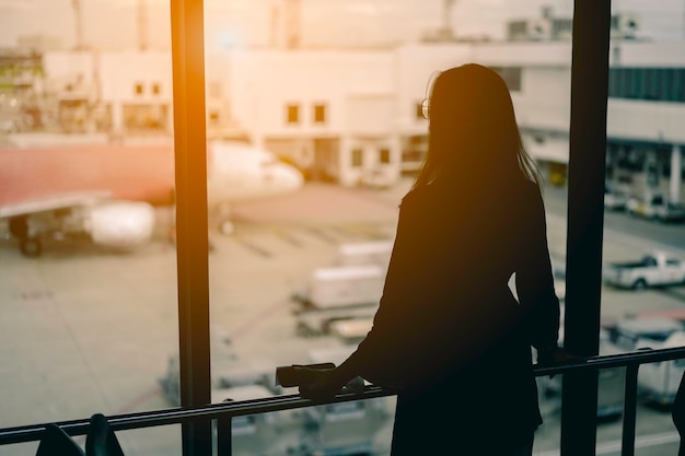 Reisefrau, die den Sonnenuntergang am Flughafenfenster beobachtet.