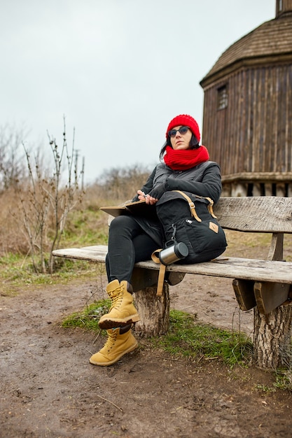Reisefrau mit rotem Hut in schwarzer Jacke auf Notizbuch schreiben, Notizen machen