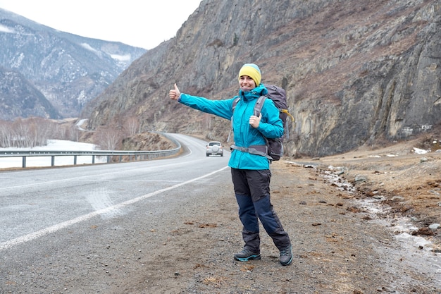 Reisefrau per Anhalter. Schöne junge Anhalterin durch die Straße während der Urlaubsreise in den Bergen