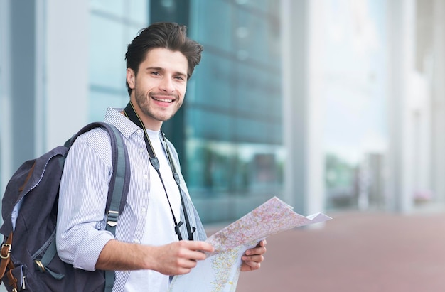 Reisekonzept für Tourismusurlaub Fröhlicher Tourist, der eine Karte in der Nähe des Flughafens hält