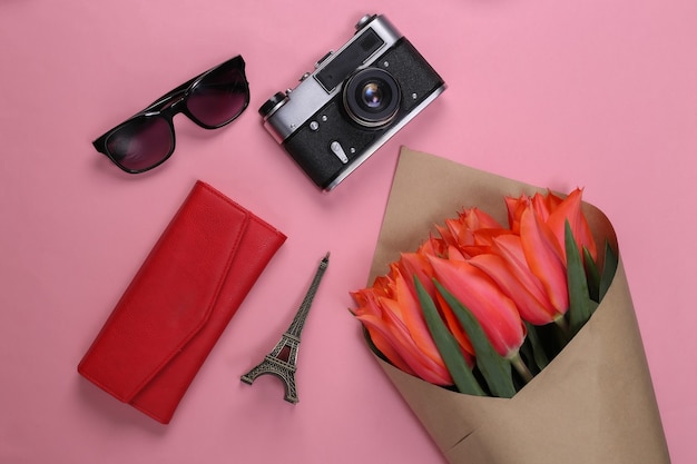 Reisekonzept. Strauß roter Tulpen, Kamera, Statuette des Eiffelturms, Sonnenbrille auf Rosa