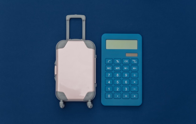 Reisekosten. Mini-Reisekoffer aus Kunststoff mit Taschenrechner auf klassischem blauem Hintergrund. Ansicht von oben. Flach legen