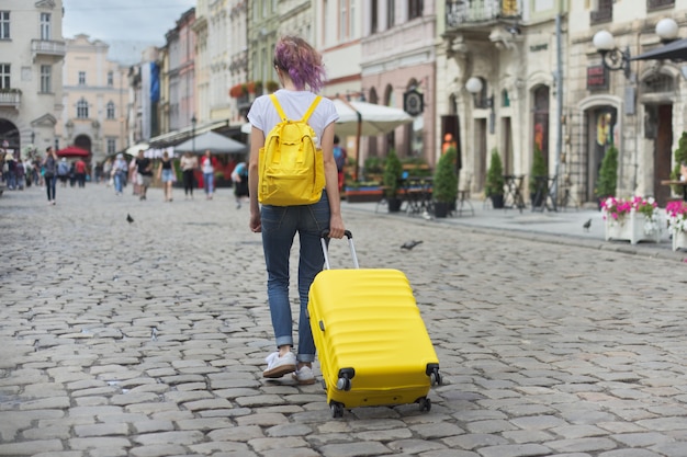 Reisemädchen, das mit Rucksack und gelbem Koffer geht