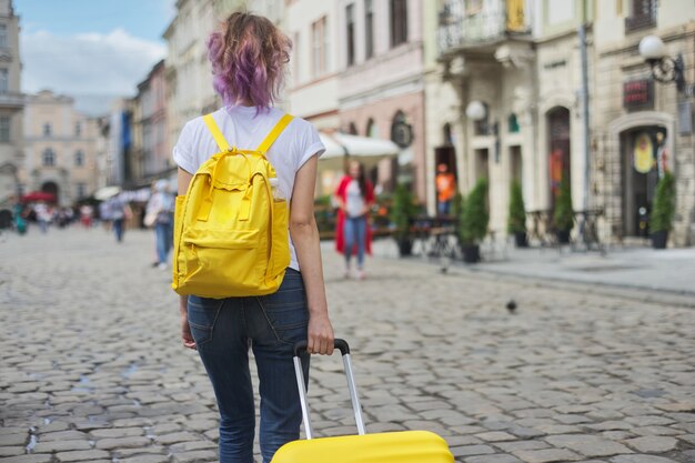 Reisemädchen, das mit Rucksack und Koffer, Rückansicht geht.