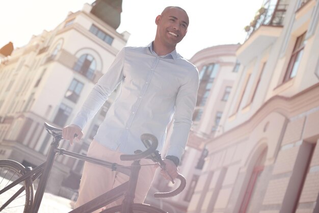 Reisen durch den jungen Mann, der mit dem Fahrrad auf der Stadtstraße spaziert und glücklich lächelt?