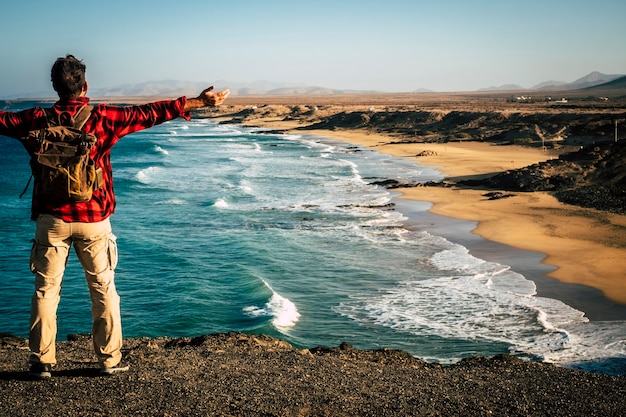 Reisen Sie für alternative Menschen Urlaub Sommerurlaub Ziel mit Mann von hinten mit einem Rucksack öffnen Arme für den Erfolg und fröhlich mit natürlichem tollen Strand vor ihm