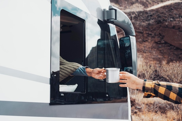 Reisen Sie mit dem Wohnmobil-Wohnmobil-Konzept Lifestyle- und Transport-Urlaubskonzept mit Seitenansicht des Fahrzeugs und der Frau, die draußen eine Tasse Kaffee an einen Mann weitergibt Konzept des Lebens außerhalb des Stromnetzes und der Freiheit