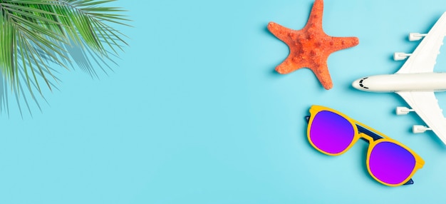 Reisen Sommer Hintergrund Sonnenbrille Palme tropische Blätter Flugzeug- und Strandzubehör auf einem farbigen...