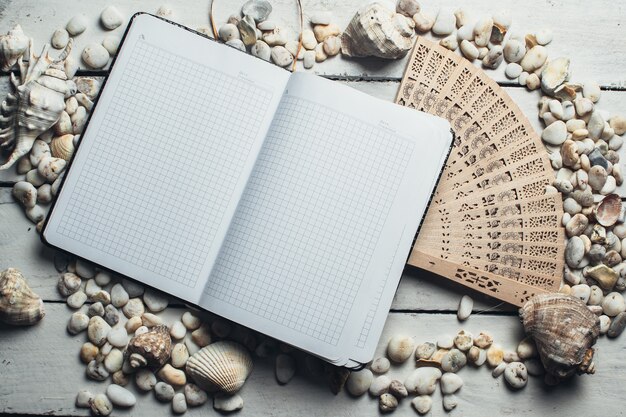 Reisen und Freizeit, auf einem Holztisch liegt ein Notizbuch neben verstreuten Muscheln