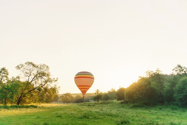 Reisen und Sport. Multi farbiger gestreifter Heißluftballon, der über Tal im Himmel bei Sonnenaufgang fliegt.