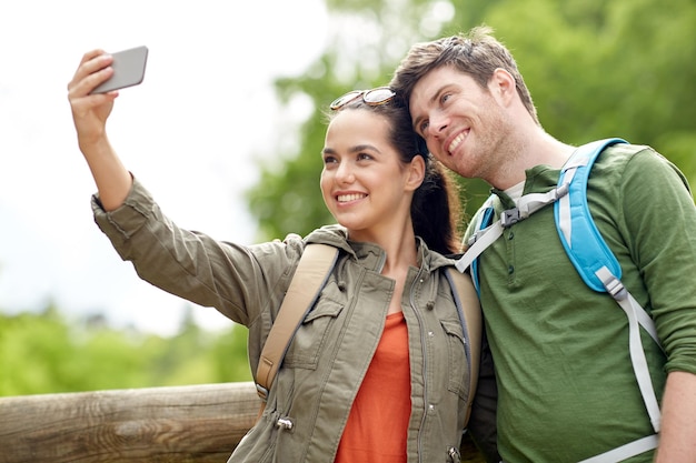 reisen, wandern, rucksackreisen, tourismus und personenkonzept - lächelndes paar mit rucksäcken, die selfie per smartphone in der natur machen