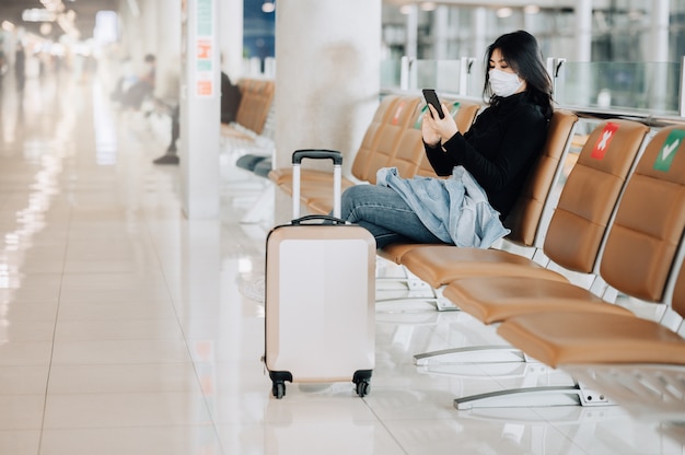 Reisende der asiatischen Frau, die Gesichtsmaske sitzt, die auf sozialem Distanzierungsstuhl sitzt