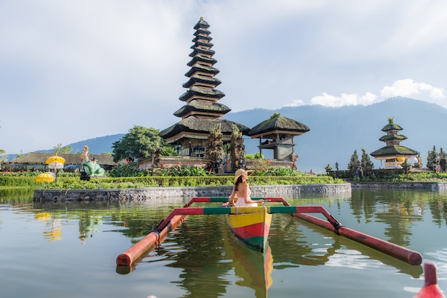 Reisende der jungen Frau, die auf einem hölzernen Boot bei Pura Ulun Danu Bratan paddelt