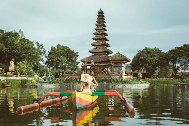 Reisende der jungen Frau, die auf einem hölzernen Boot bei Pura Ulun Danu Bratan paddelt