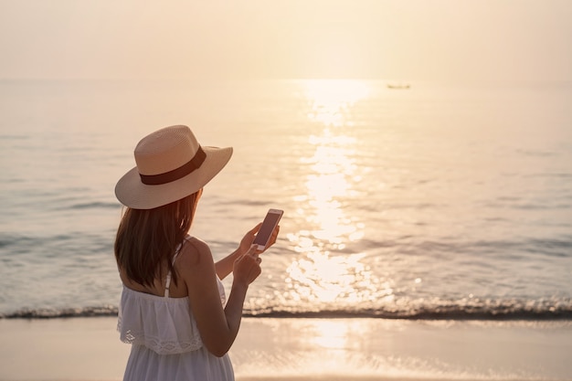 Reisende der jungen Frau, die Handy am tropischen Strand bei Sonnenuntergang verwendet