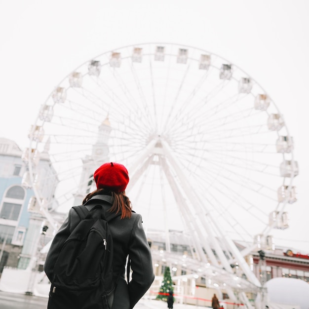 Reisende der jungen Frau im roten Hut und im schwarzen Mantel, die draußen das Riesenrad in Kiew-Ukraine betrachten