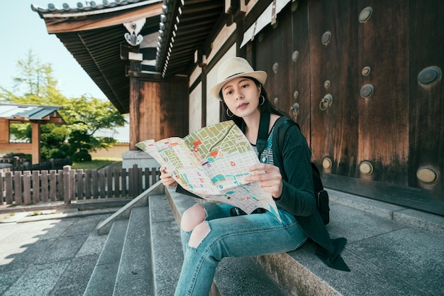 Reisende der jungen Frau mit Rucksack und Hut, die Papierkarte im Shitennoji-Tempel Osaka Japan schauen. In den Sommerferien durch Asien reisen. entspannte Besucherin im Schrein, die auf einer Felsentreppe sitzt und denkt.