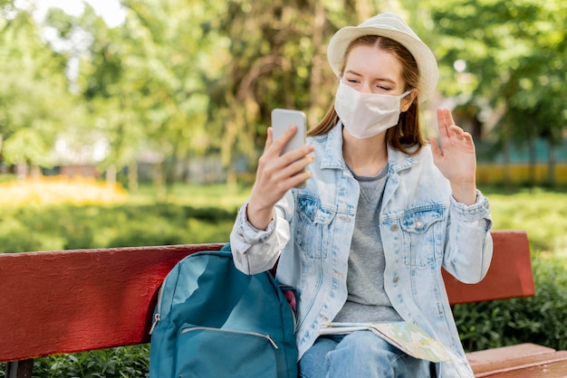 Reisende, die medizinische Maske mit ihrem Telefon i trägt