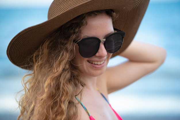 Reisende Frau am Strand mit blonden Haaren, Hut und Sonnenbrille.