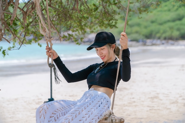 Reisende Frau im Badeanzug entspannt auf Schaukel unter Baum suchen Meeresstrand.