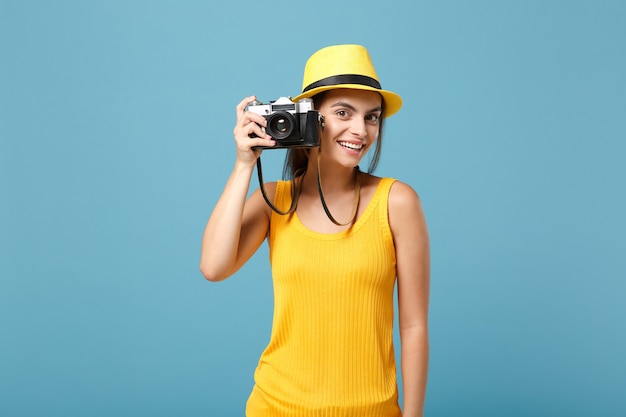 Reisende Frau in gelber Sommerkleidung und Hut mit Fotokamera auf Blau