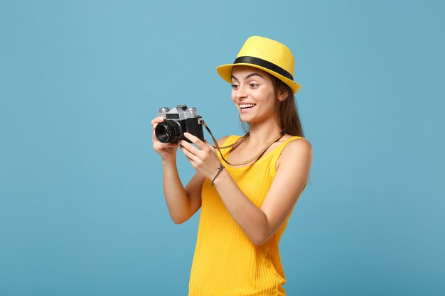 Reisende Frau in gelber Sommerkleidung und Hut mit Fotokamera auf Blau