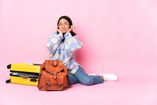 Reisende Frau mit einem Koffer, der frustriert auf dem Boden sitzt und Ohren bedeckt