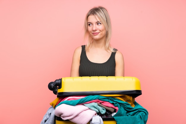 Reisende Frau mit einem Koffer voller Kleider stehend und zur Seite schauend