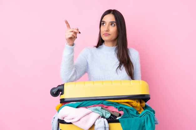 Reisende Frau mit einem Koffer voller Kleidung über isolierte rosa Wand, die auf transparentem Bildschirm berührt