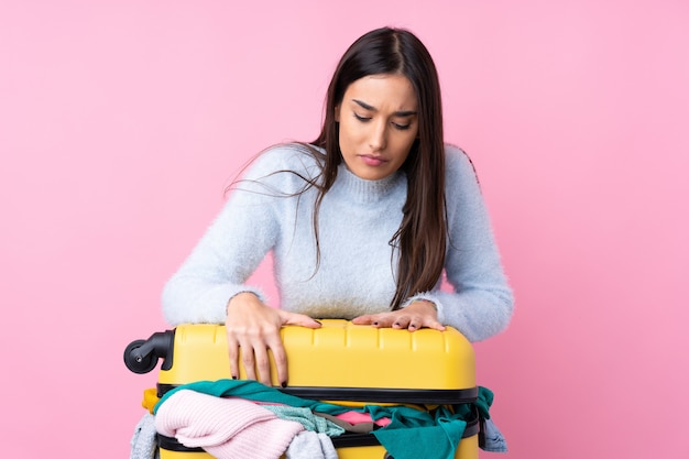 Reisende Frau mit einem Koffer voller Kleidung über rosa