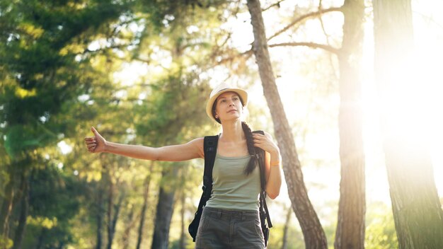 Reisende Frau per Anhalter auf einer sonnigen Waldstraße Touristische Mädchen auf der Suche nach Fahrt, um ihre Reise zu beginnen