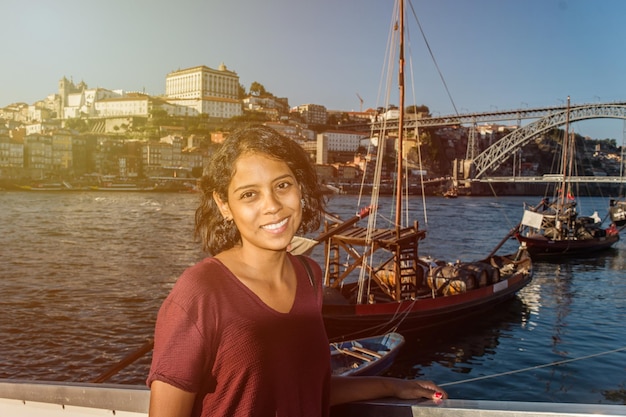 Reisende Frau posiert in der Nähe des Flusses mit alten Booten und der Skyline der Stadt im Hintergrund Frau, die Porto und den Fluss Douro genießt