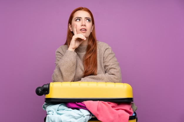 Reisende junge Frau mit einem Koffer voller Kleider, die eine Idee denken