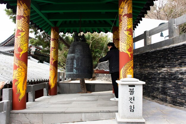 Reisende koreanische Männer reisen besuchen und klopfen an die alte große Eisenmetallglocke, um am 18. Februar 2023 im Sanbangsa-Tempel in Seogwipo auf der Insel Jeju Do in Südkorea den Wunsch zu beten