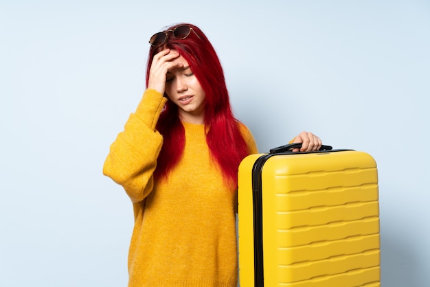 Reisende Mädchen, die einen Koffer lokalisiert auf Blau mit Kopfschmerzen hält