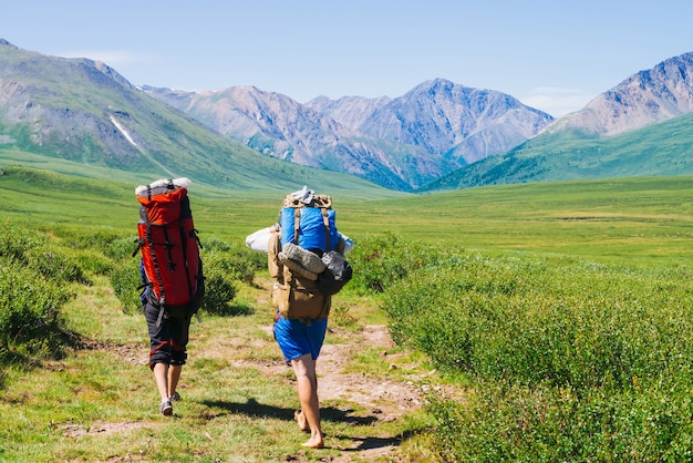 Reisende mit großen Rucksäcken begeben sich auf einen Wanderweg im grünen Tal zu wunderschönen Riesenbergen