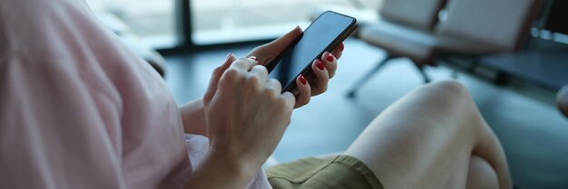 Reisende mit Smartphone in der Hand sitzt im Abflugbereich am Flughafen oder Bahnhof